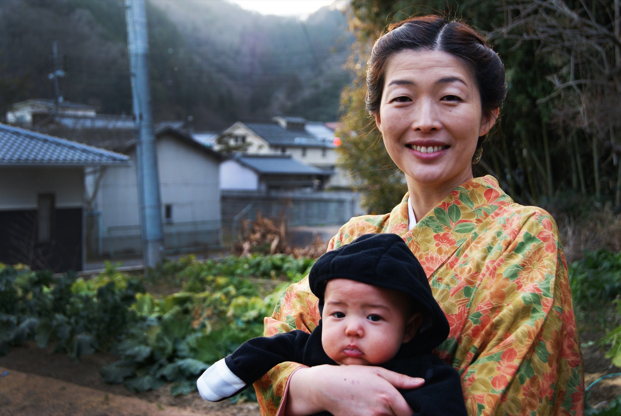 Aya in a kimono holding baby Kai in the garden